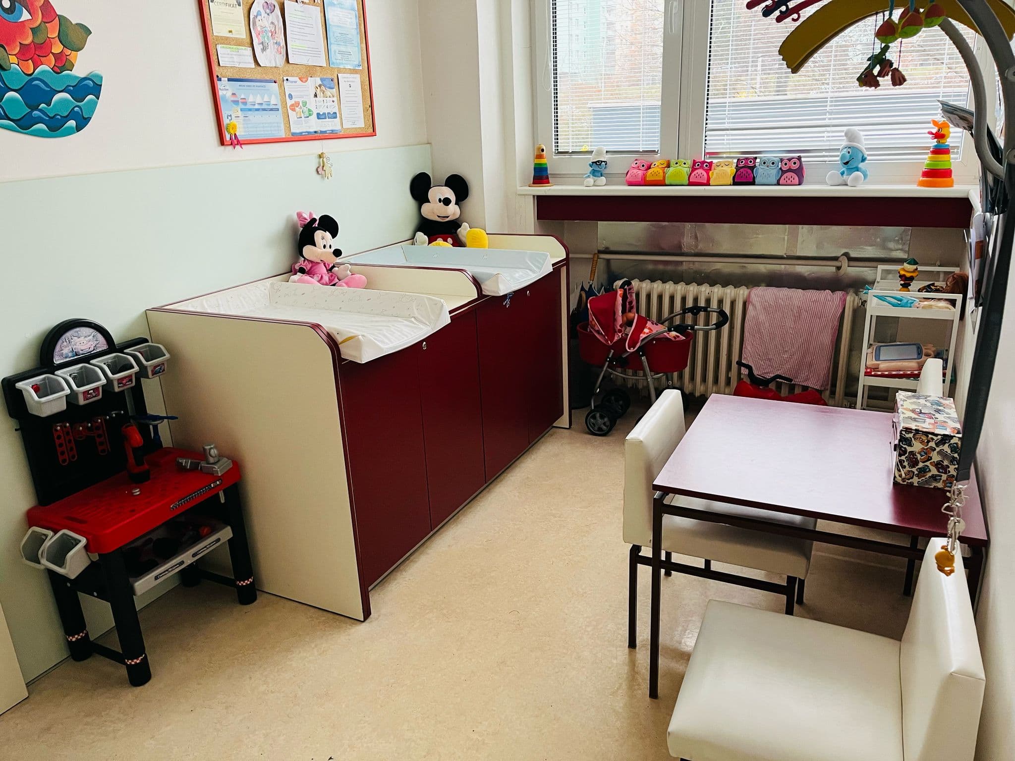 Místnost v dětské ordinaci s přebalovacím pultem, na kterém jsou plyšové hračky Mickey a Minnie Mouse.